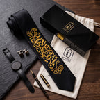 Black KHOMAR-E-MASTI necktie with gold calligraphy laid on slate beside its gift box, dust bag, watch and cufflinks