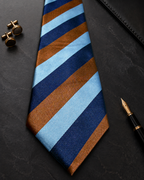 Navy necktie with sky blue and bronze stripes beside gold cufflinks and a fountain pen