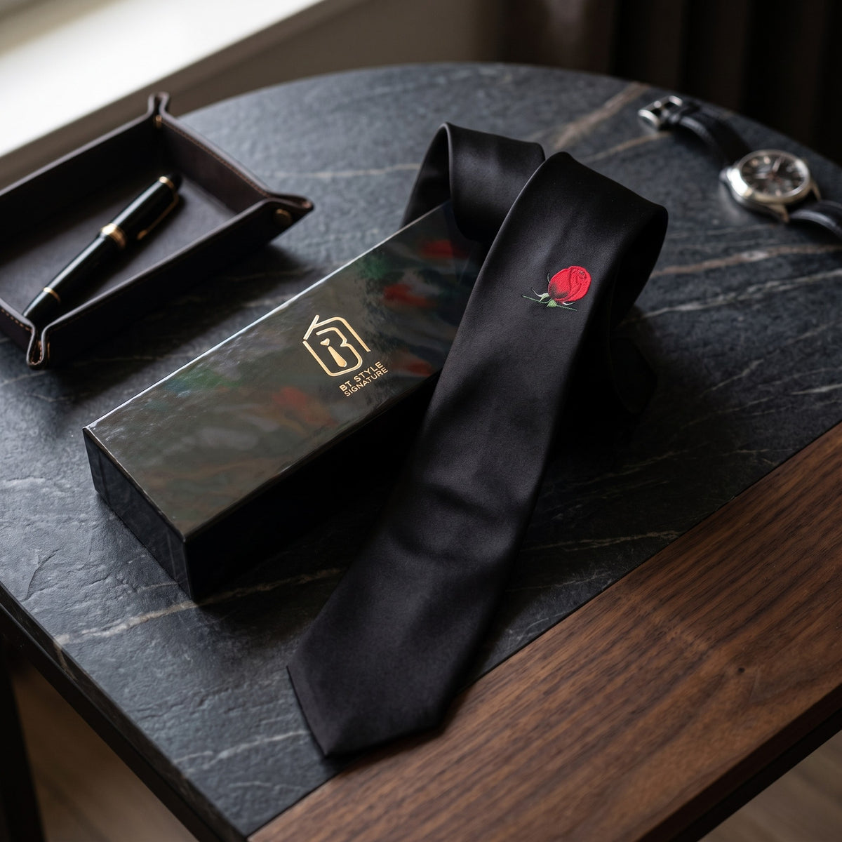 Red Rose black satin necktie with gift box, pen tray and watch on a marble desk